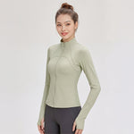 Woman wearing a light green FormFlex_High-Neck_Jacket and dark gray leggings on a white background