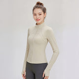 Woman wearing a beige FormFlex_High-Neck_Jacket and gray leggings on a light gray background