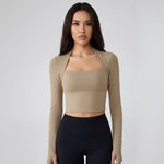 Woman wearing a SoftForm_Long-Sleeve_Yoga_Top_taupe long-sleeve top and black leggings on a gray background