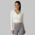 Woman wearing a white SoftForm™ V-Neck Long-Sleeve Hoodie and gray leggings on a gray background