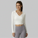 Woman wearing a white SoftForm™ V-Neck Long-Sleeve Hoodie and gray leggings on a gray background