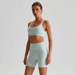 Woman wearing a teal SoftForm™ Yoga Set bra and shorts set in teal on a light gray background