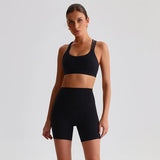 Woman wearing a SoftForm™ Yoga Set_black sports bra and shorts on a light gray background