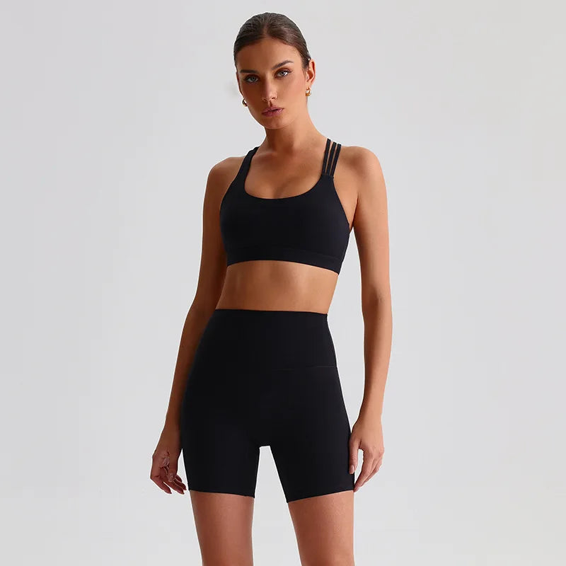 Woman wearing a SoftForm™ Yoga Set_black sports bra and shorts on a light gray background