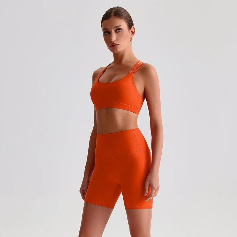 Woman wearing an SoftForm™ Yoga Set_orange sports bra and shorts set on a light gray background