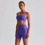 Woman wearing a SoftForm™ Yoga Set_violet sports bra and shorts set on a light gray background