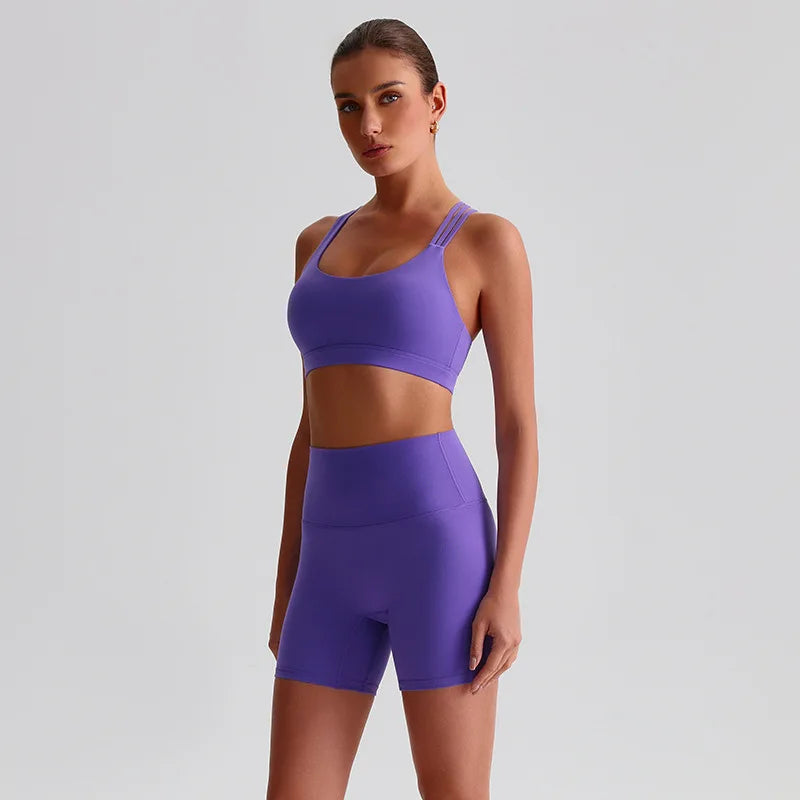 Woman wearing a SoftForm™ Yoga Set_violet sports bra and shorts set on a light gray background