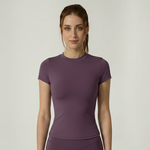 Woman wearing a purple SoftForm_Yoga_Shirt athletic outfit on a plain background