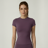 Woman wearing a purple SoftForm_Yoga_Shirt athletic outfit on a plain background
